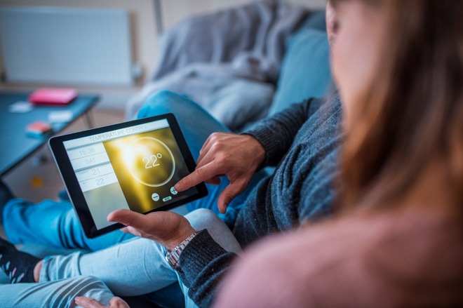 A couple adjust the temperature of their home on their tablet, from the comfort of their sofa